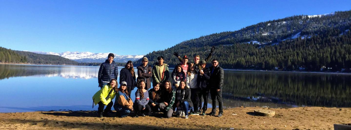 A group of students stand on a lake bank in winter.