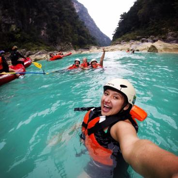 Desirae takes a selfie in turqouise waters with a life jacket, rafting helmet, and friends in the background