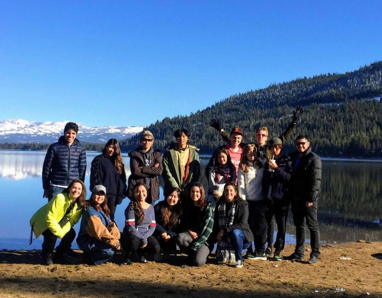 A group of students stand on a lake bank in winter.