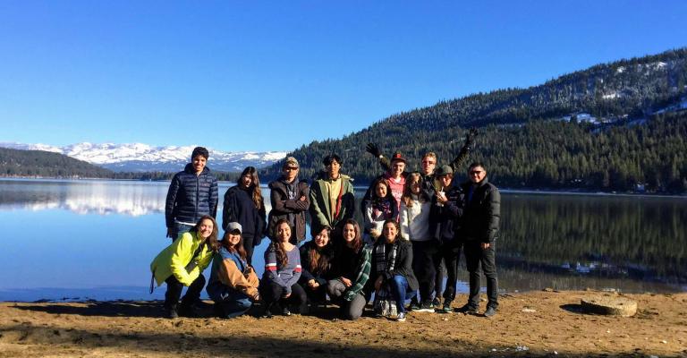 A group of students stand on a lake bank in winter.