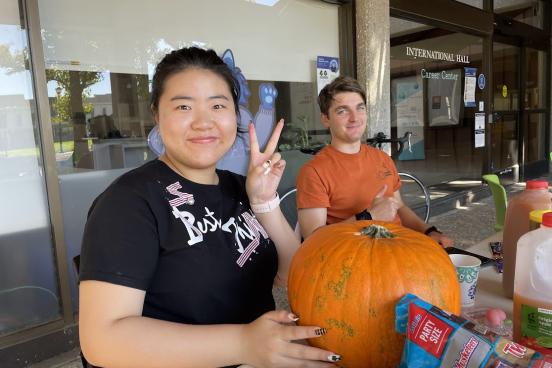two smiling friends carving pumkins