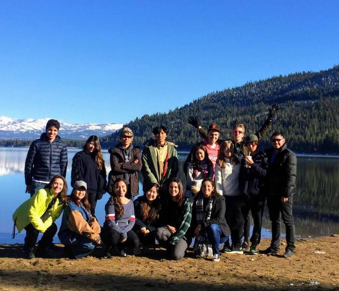 A group of students stand on a lake bank in winter.