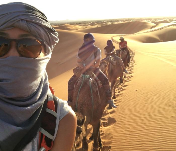 Student with sunglasses takes selfie with other students behind her on camels