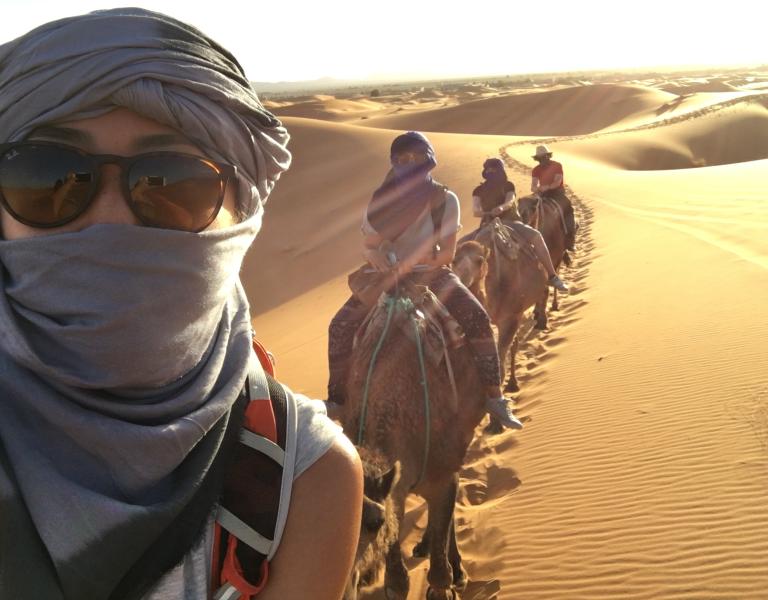 Student with sunglasses takes selfie with other students behind her on camels