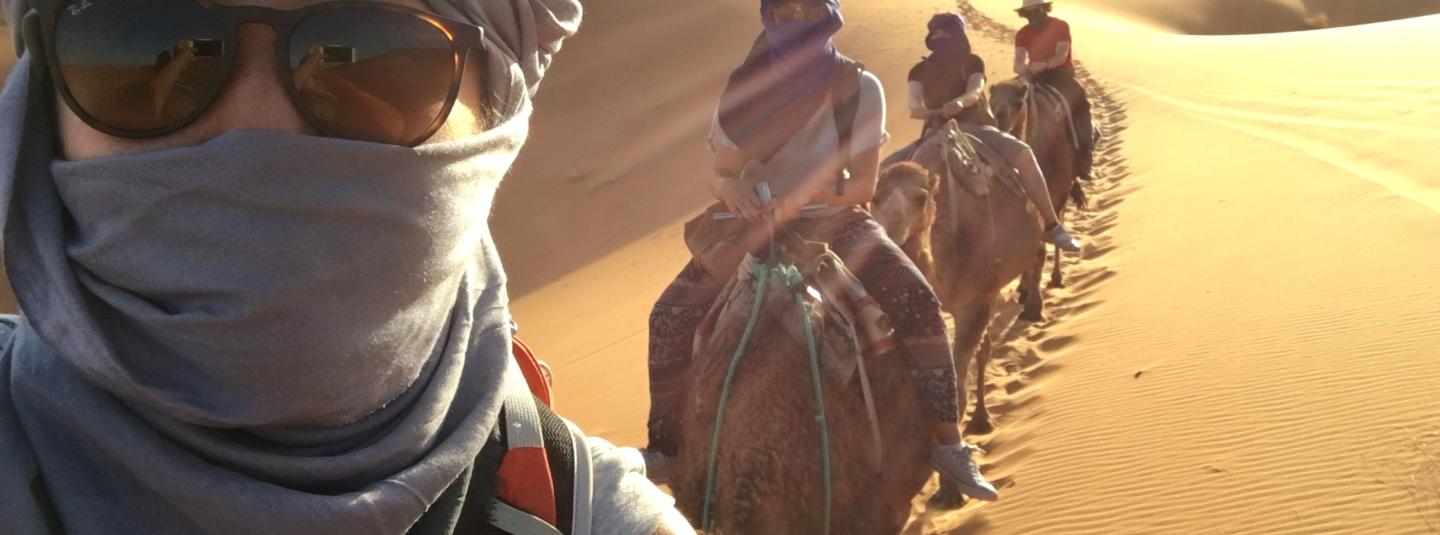 Student with sunglasses takes selfie with other students behind her on camels