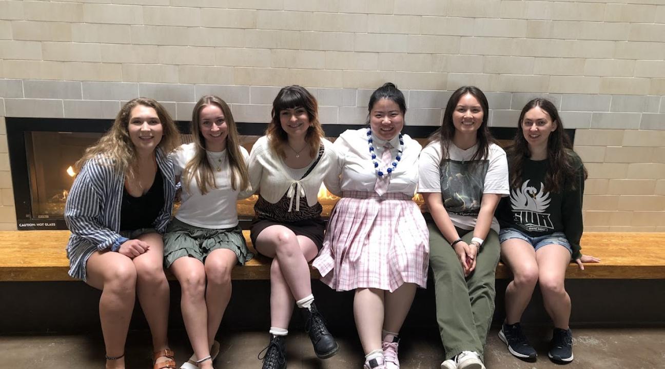 Six ladies sitting on bench near fireplace smiling