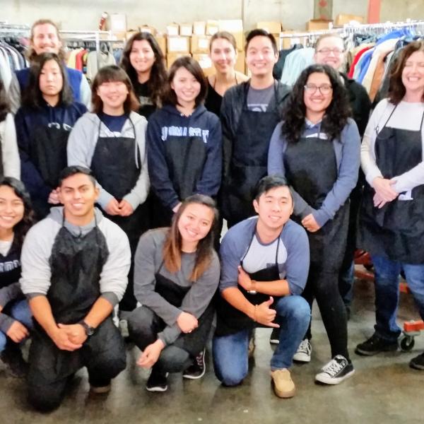 Students in aprons around clothes wracks. 