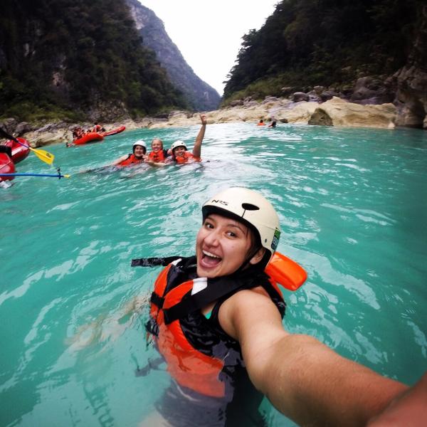 Desirae takes a selfie in turqouise waters with a life jacket, rafting helmet, and friends in the background