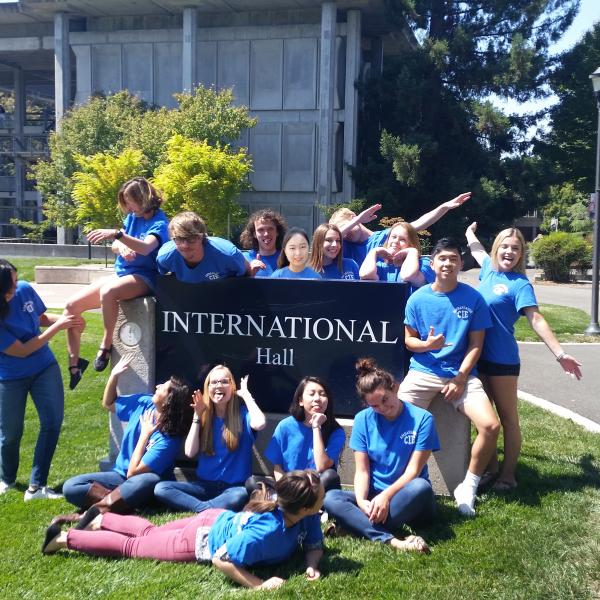 Group of ambassadors acting silly around International Hall sign.