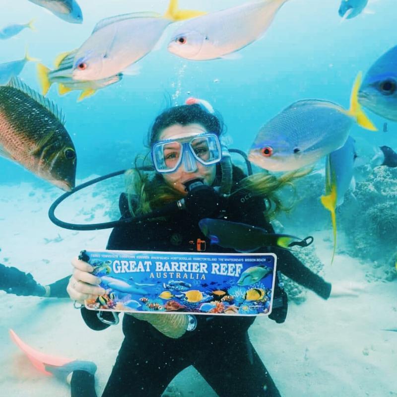 Girl underwater, scuba diving while surrounded by fish, hold sign saying Great Barrier Reef, Australia.