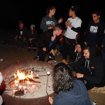 Students cook marshmallows around a campfire. 