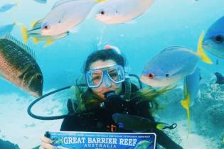 Girl underwater, scuba diving while surrounded by fish, hold sign saying Great Barrier Reef, Australia.