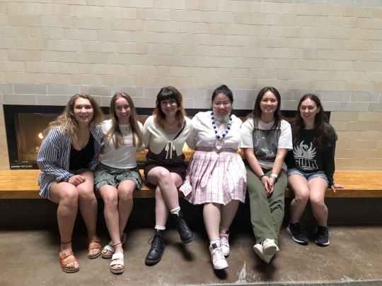 Six ladies sitting on bench near fireplace smiling
