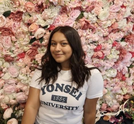 Gloria stands in front of a wall of roses with Yonsei University t-shirt on